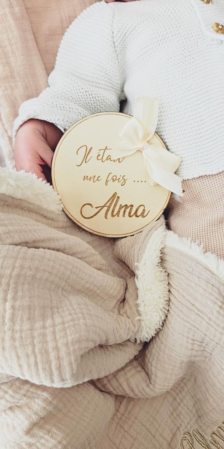 Carte de présentation naissance ronde en bois gravé avec prénom personnalisé et grand nœud en satin crème, style bohème chic.